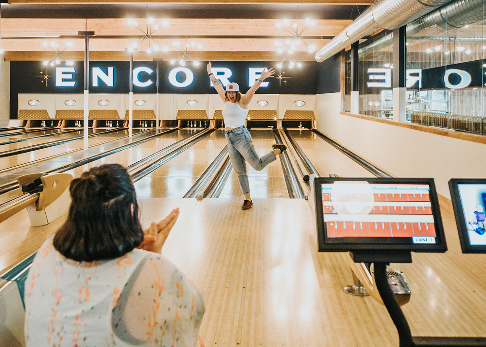 A woman having fun bowling while another woman claps.