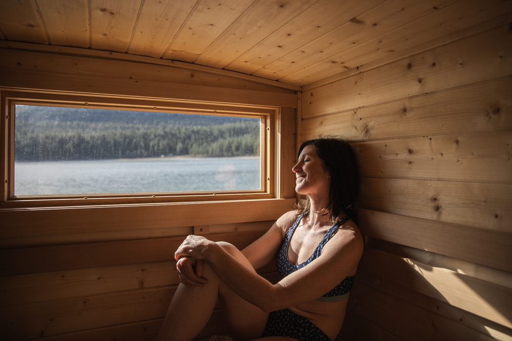 A woman relaxing in a sauna with a window view of a forested area